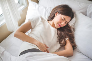 Woman laying in bed with abdominal pain caused by appendicitis