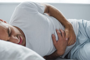 Man laying in bed clutching his stomach due to abdominal pain caused by appendicitis
