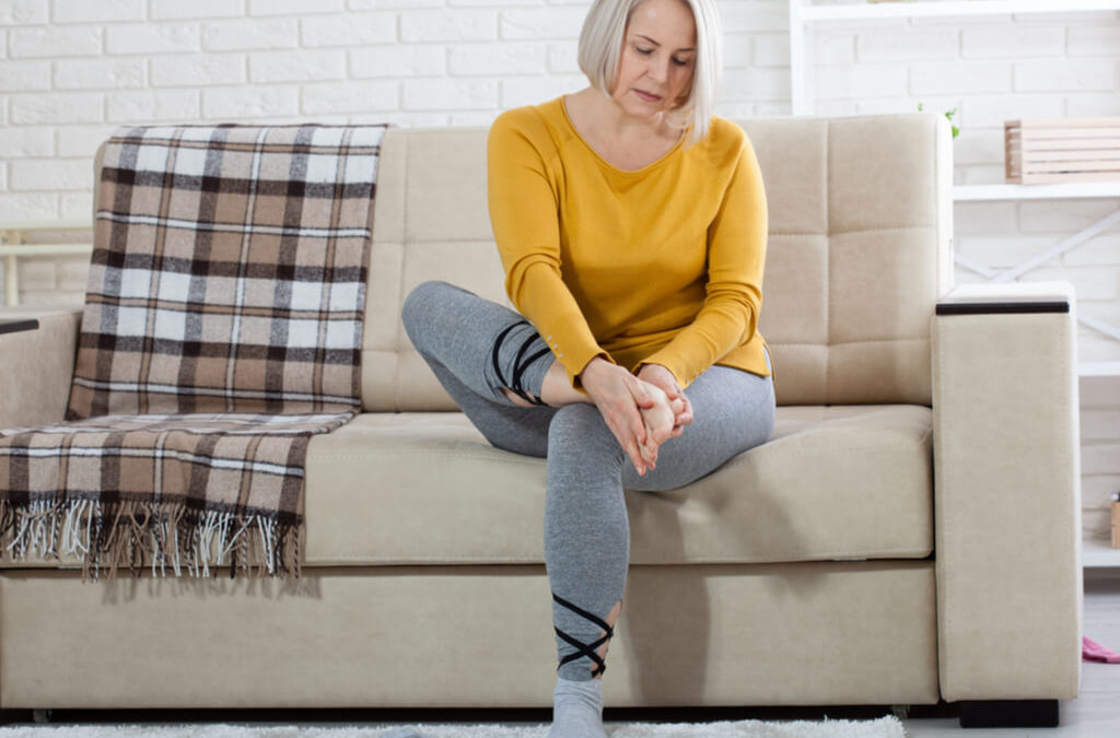 A woman sitting on a couch with foot pain.