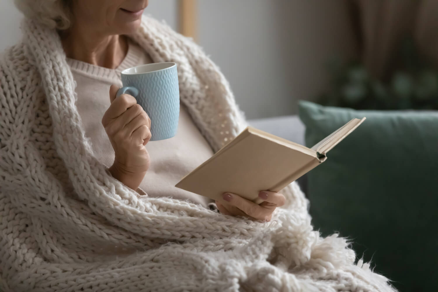 A woman recovering from vascular surgery in the winter, laying in bed with a cozy blanket, a cup of tea, and reading a book.