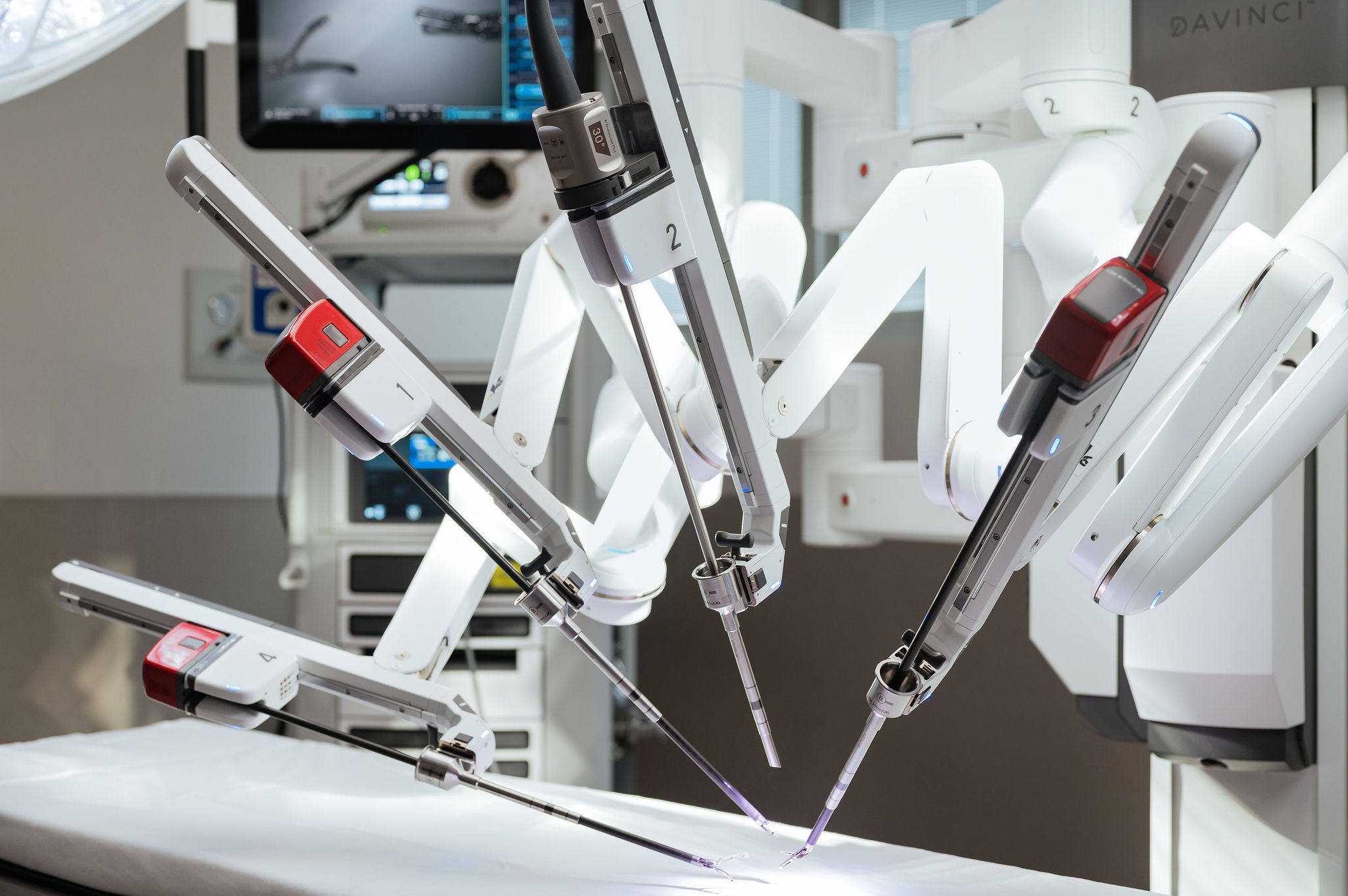 An example of the davinci surgical robot. The four arms of the device are focused on the surgery table, and in the background a visual display console can be seen. No one is in the room.