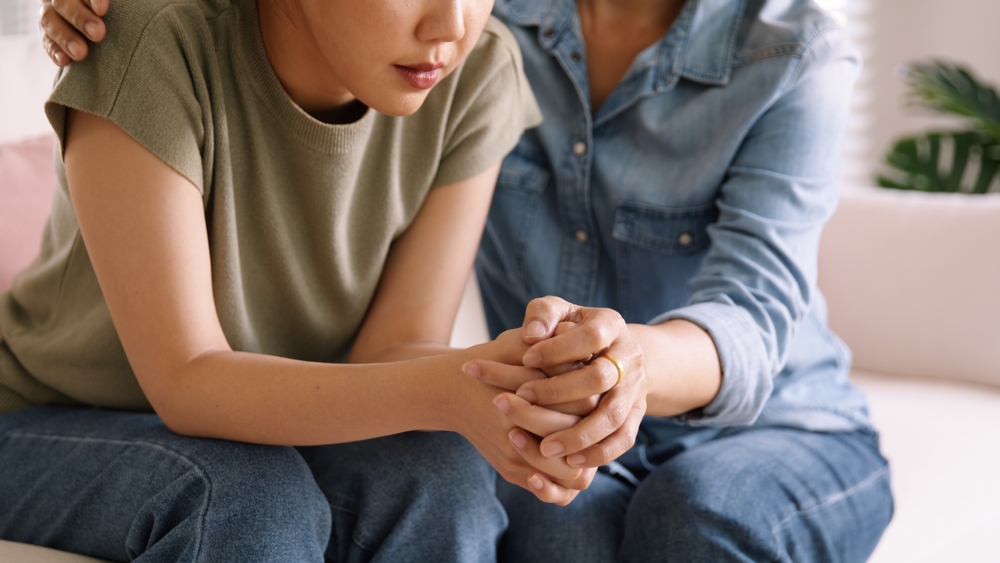 woman holding hand of other woman in somber sense