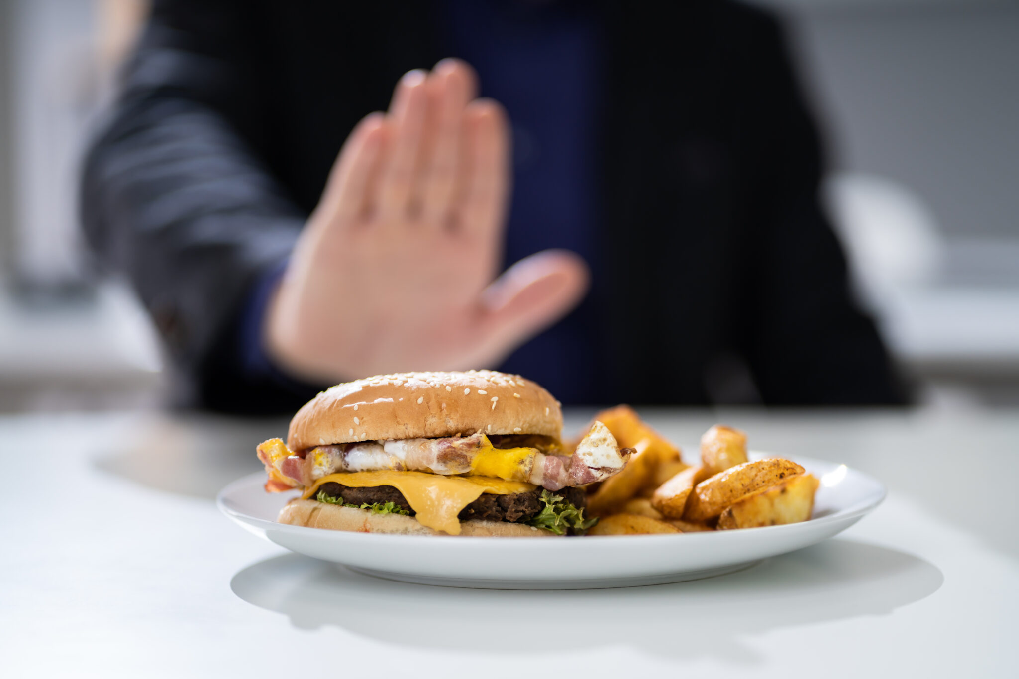 Hand pushing away plate of fries and burgers.