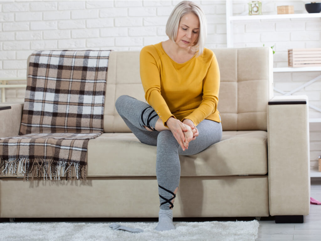 A woman sitting on a couch with foot pain.